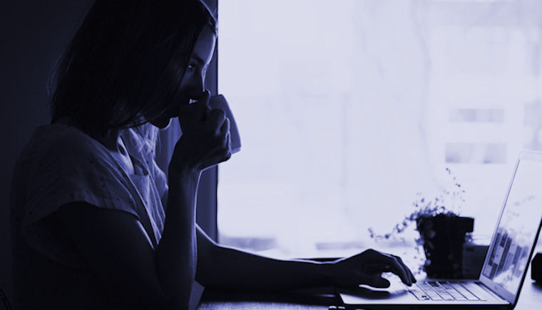 Photo of a woman drinking coffee whilst working on a laptop